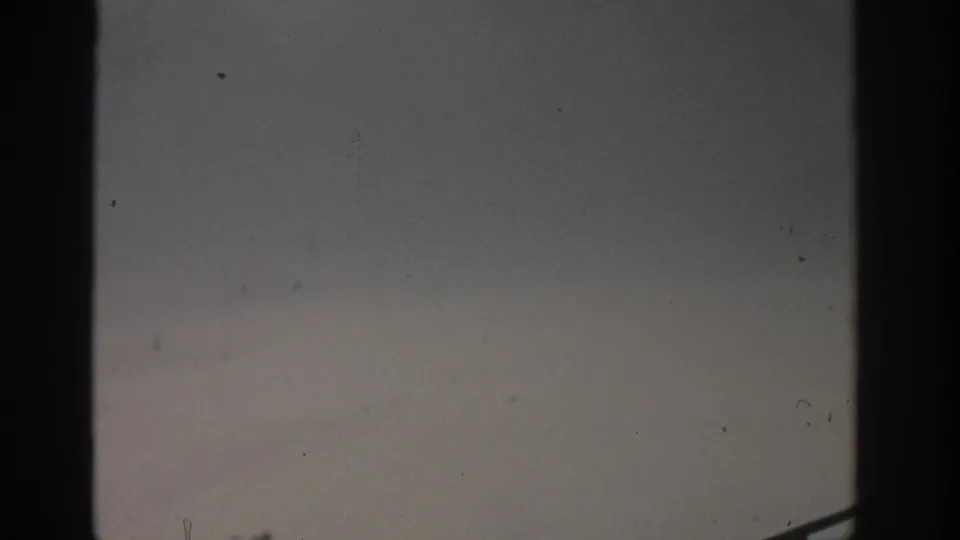 1963 Munich 8mm frame showing hazy overcast sky, visible film wear, and the edge of a metal railing.