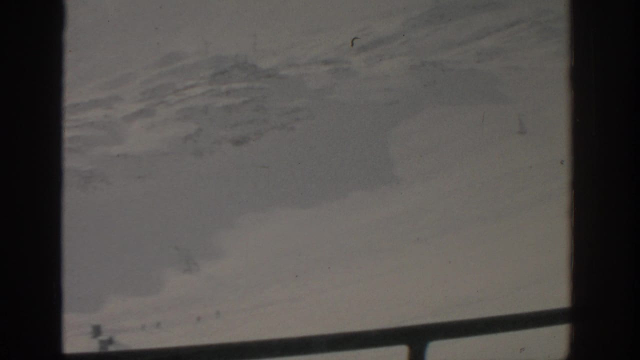 1963 8mm home-movie view near Munich showing a snowy slope, faint tracks, and a tiny skier partly obscured by frame borders.