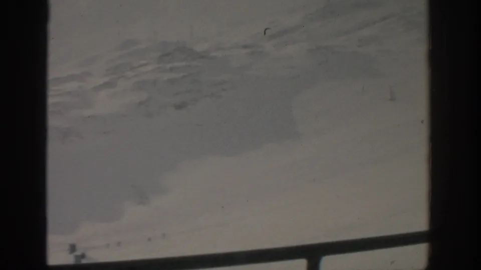 1963 8mm home-movie view near Munich showing a snowy slope, faint tracks, and a tiny skier partly obscured by frame borders.