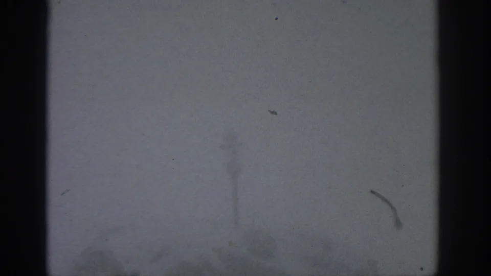 1963 Munich-attributed 8mm frame showing dense fog, a dark vertical edge, and barely visible distant forms.