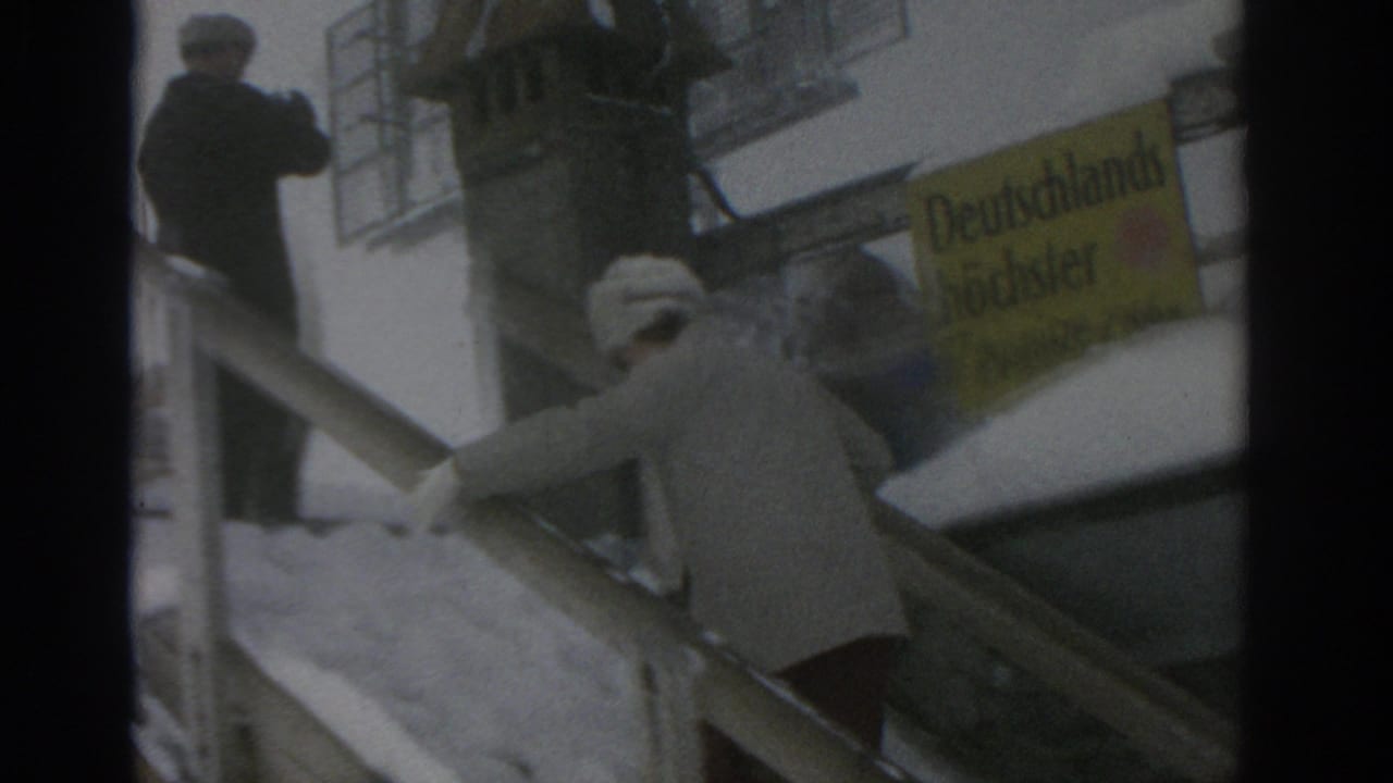 Bundled adults climb snowy outdoor stairs beside a yellow German sign.