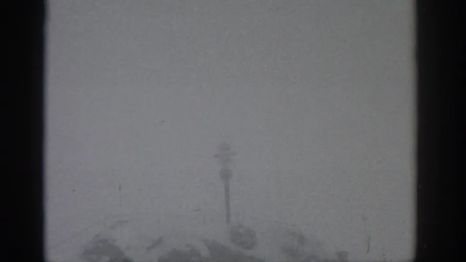 Overexposed 8mm frame with faint snowy outdoor forms, soft grain, and small film specks visible.