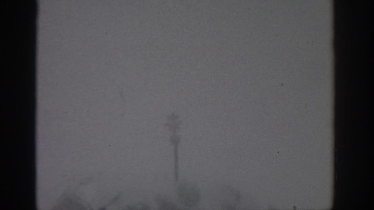 Soft, gloomy 8mm frame from Munich showing a window view with dark mullions and faint exterior shapes on an overcast day.