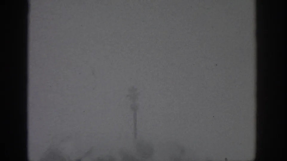 Soft, gloomy 8mm frame from Munich showing a window view with dark mullions and faint exterior shapes on an overcast day.