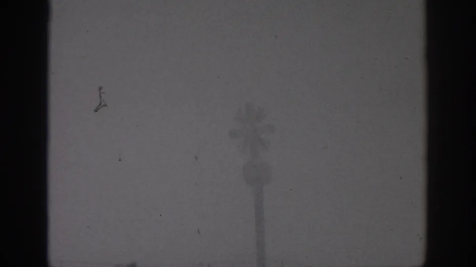 Munich 1963 home-movie frame looking through dark interior framing toward a hazy palm-like silhouette outside.