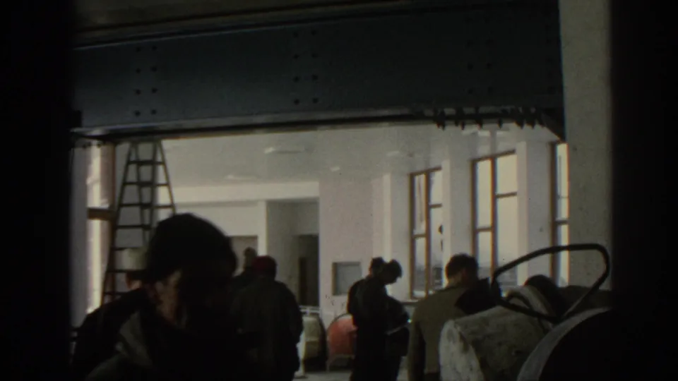 Munich 1963 8mm frame of men working inside a dim building under renovation, with a ladder, beams, and open windows visible.
