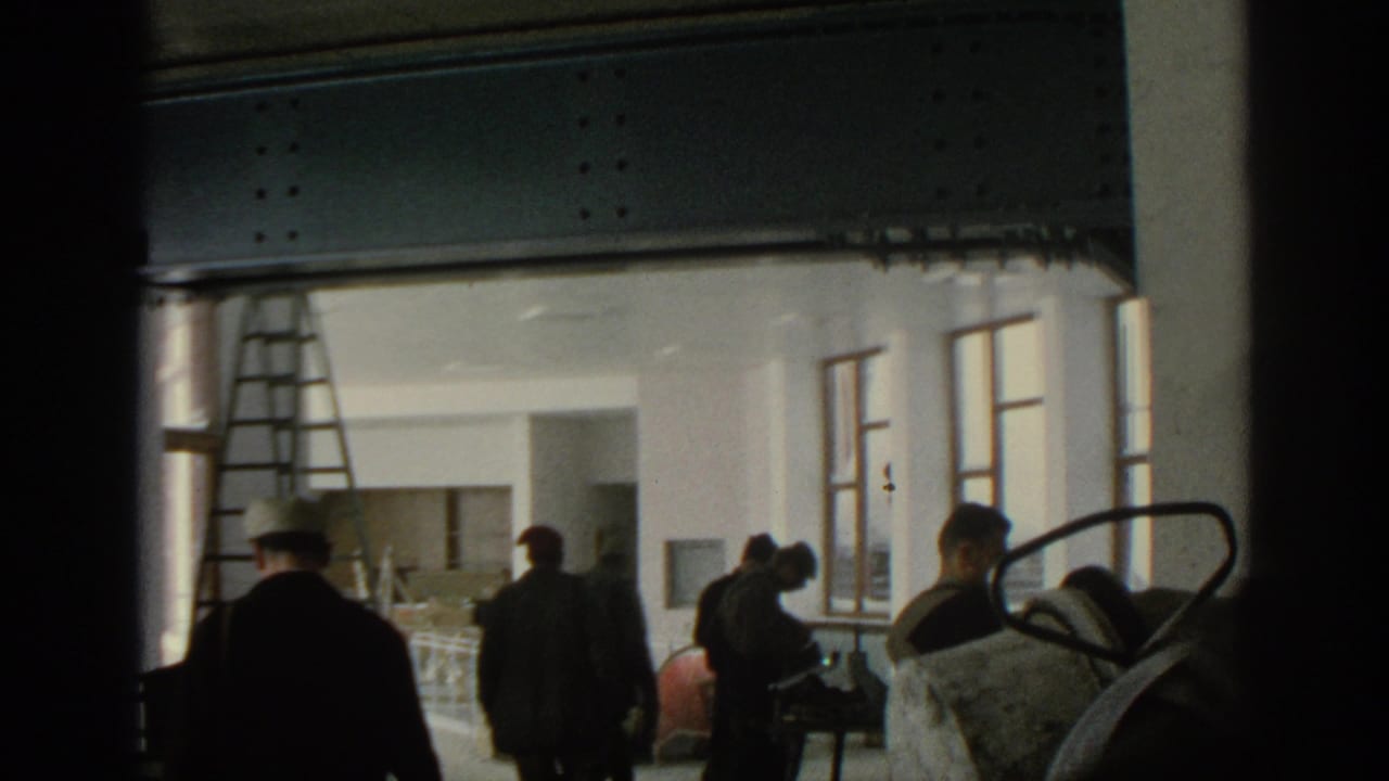 Workers and visitors seen through a doorway inside an unfinished building with ladder and exposed ceiling.