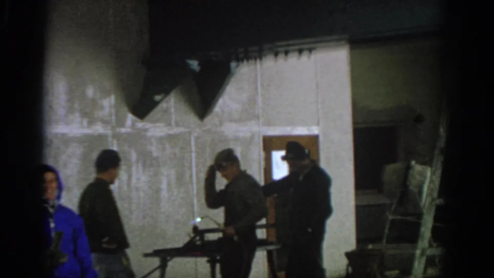 Munich 1963 frame of adults moving near a doorway and work light inside an unfinished private interior.