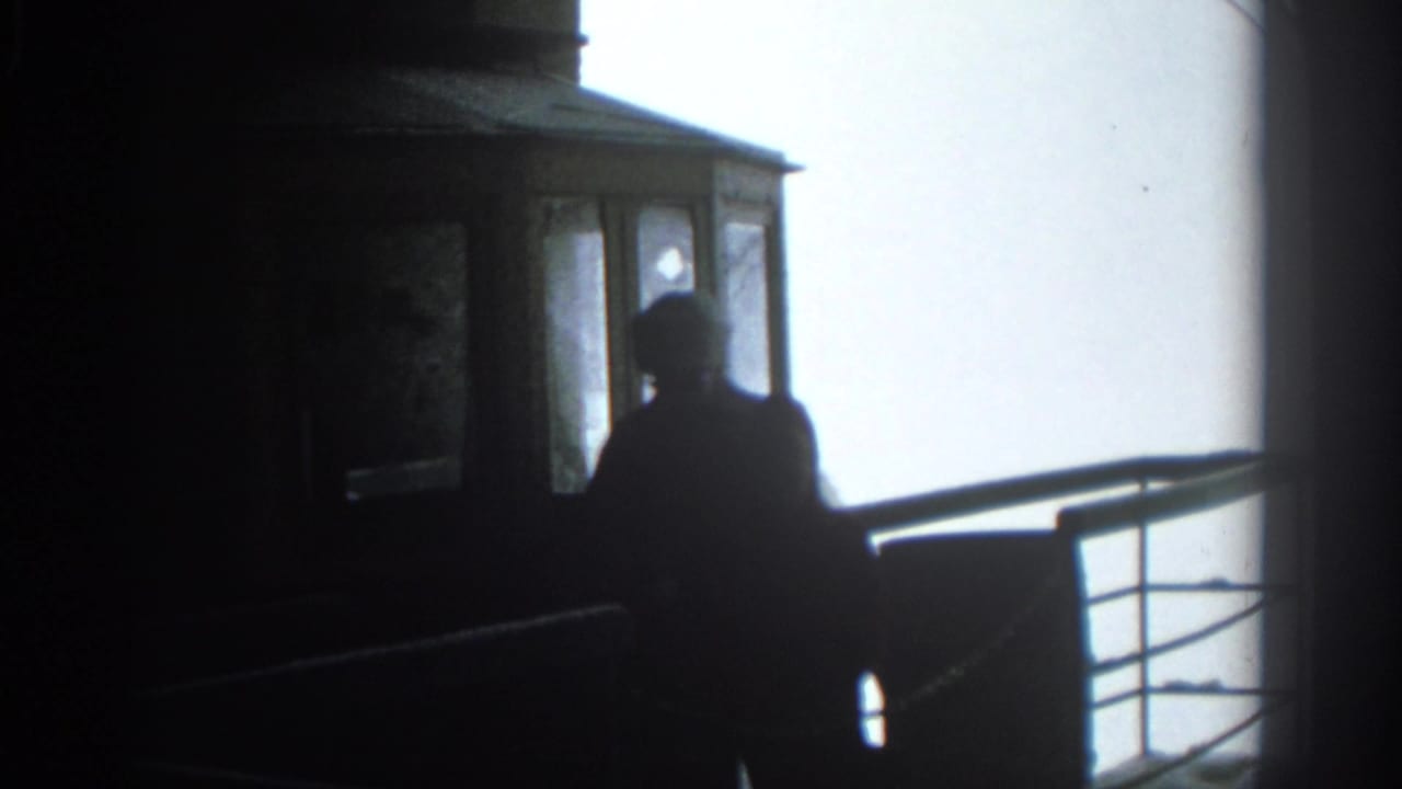 Two silhouetted figures stand inside a dark tram cab beside windows and a rail.
