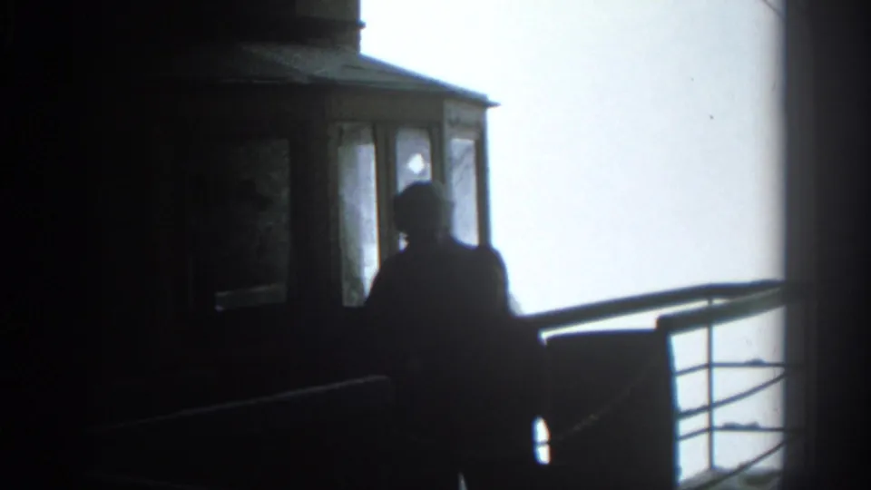 In 1963 Munich, two silhouetted people stand in a dim tram cabin against a bright overcast sky.