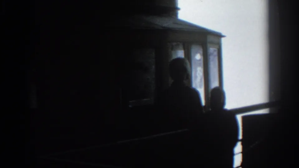 The 8mm frame shows Munich tram passengers or visitors in silhouette near glass panels and a slanting rail.