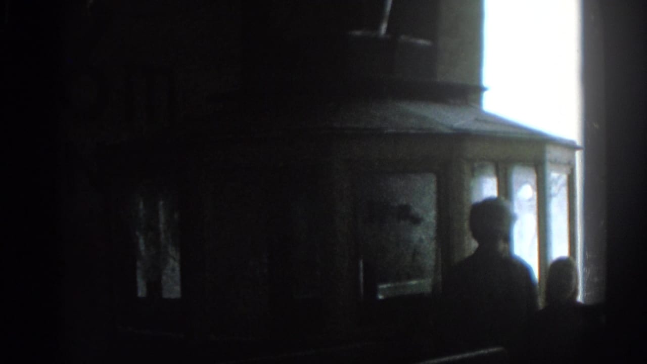 Silhouetted people stand or sit near a bright rectangular light in a dark interior.