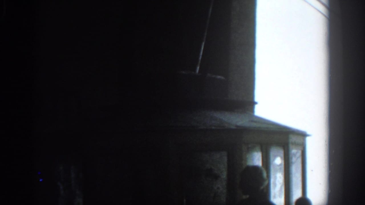 Dark room with a bright window or screen edge and partial silhouettes at the lower right.