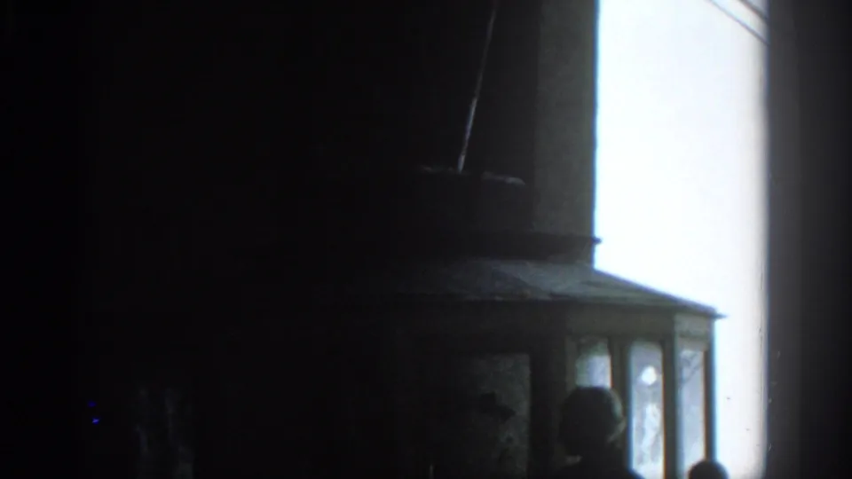 A dim Munich 1963 interior shows a bright vertical screen or window with partial viewer silhouettes near the edge.