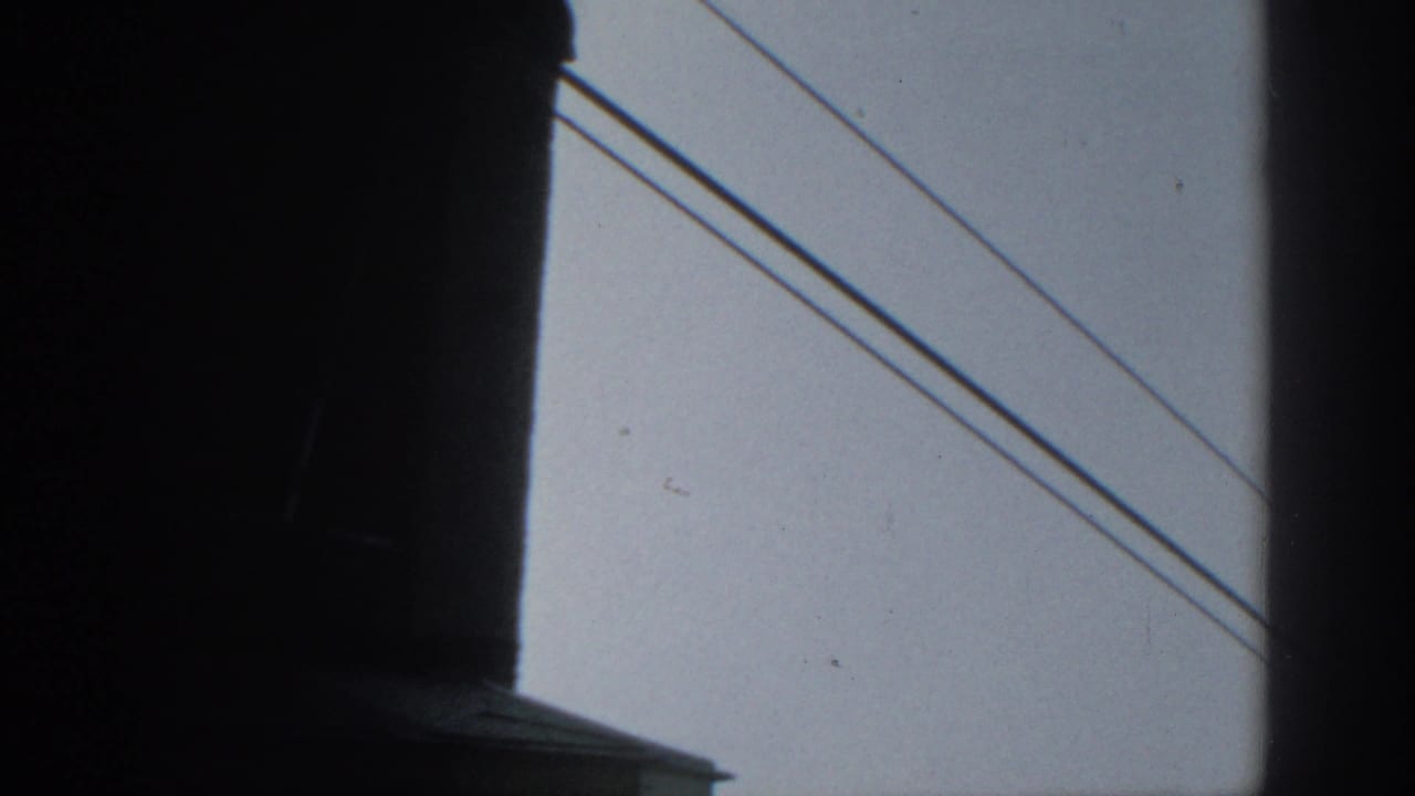 1963 Munich home-movie frame showing silhouetted foreground structure and power lines crossing a gray sky.