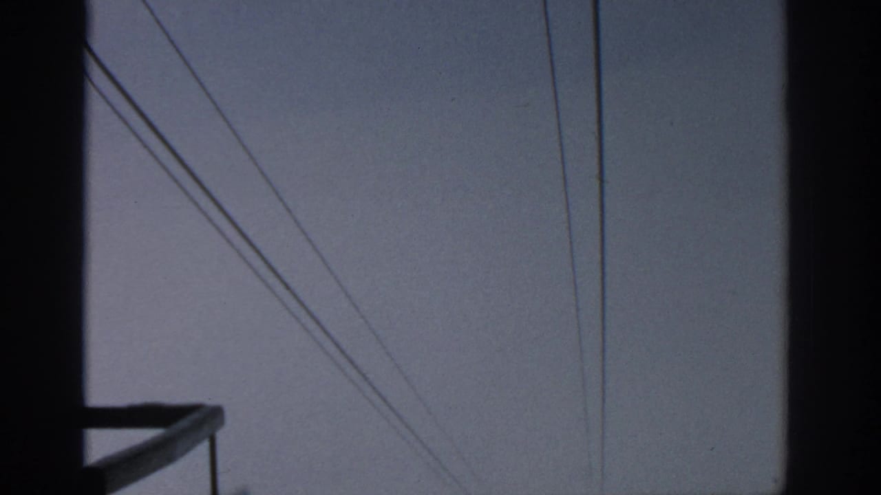 Silhouetted vertical frame, small platform edge, and power lines in a gray sky.