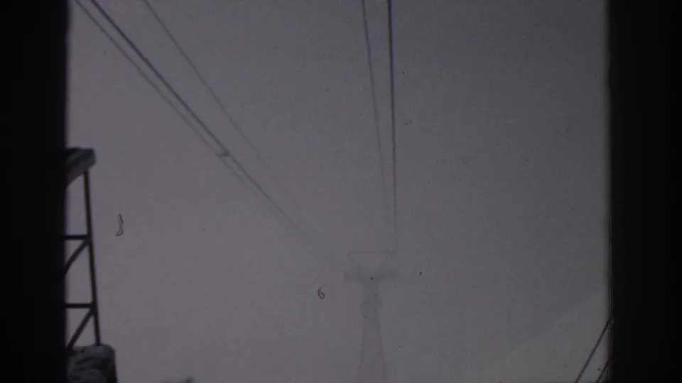 Muted 1963 Munich view of a distant electrical tower and overhead lines, partly framed by a dark structure.