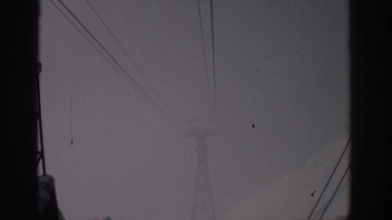 1963 8mm view near Munich showing a hazy snow-covered mountain partly obscured by dark structures and wires.