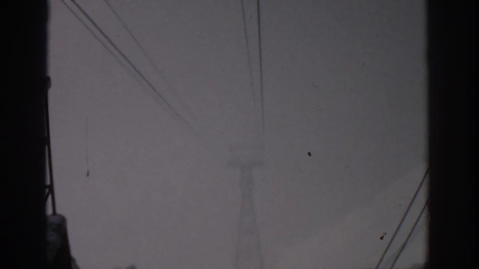 1963 8mm view near Munich showing a hazy snow-covered mountain partly obscured by dark structures and wires.