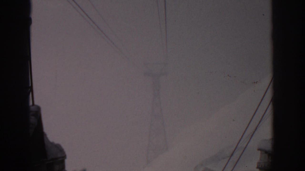 Hazy snowy mountain and a faint transmission tower seen behind dark foreground structure.