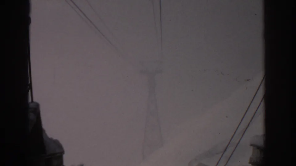 1963 8mm frame near Munich with a faint power line tower and snow-covered mountain softened by fog.