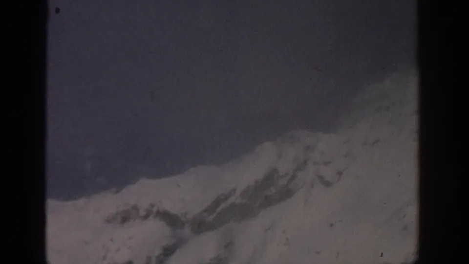 1963 8mm mountain landscape near Munich, with snowy slopes below a gray fog-softened sky.