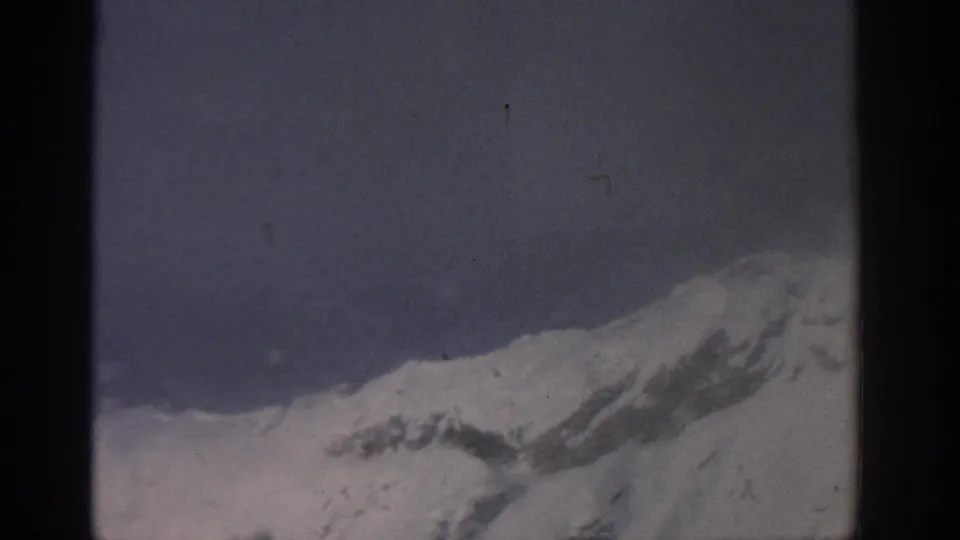 1963 8mm frame near Munich showing a snowy ridge and distant utility tower softened by mist.