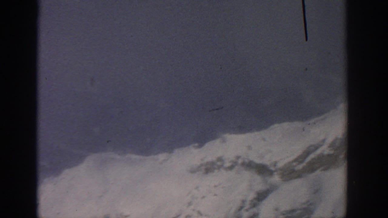 Snow-covered mountain ridge beneath pale blue sky with dark film-frame borders.