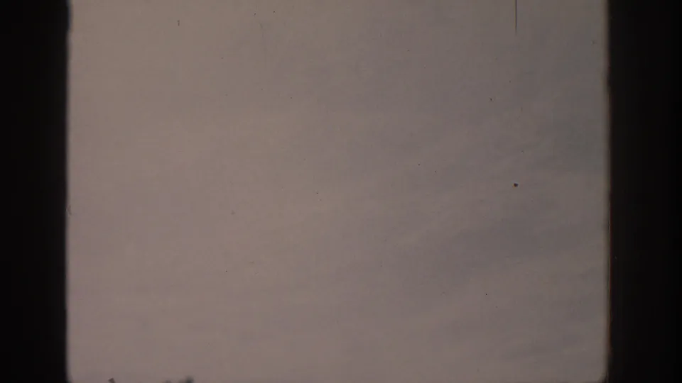 Faded 8mm frame from an aircraft view, showing muted snow-covered terrain and prominent dark film-frame edges.