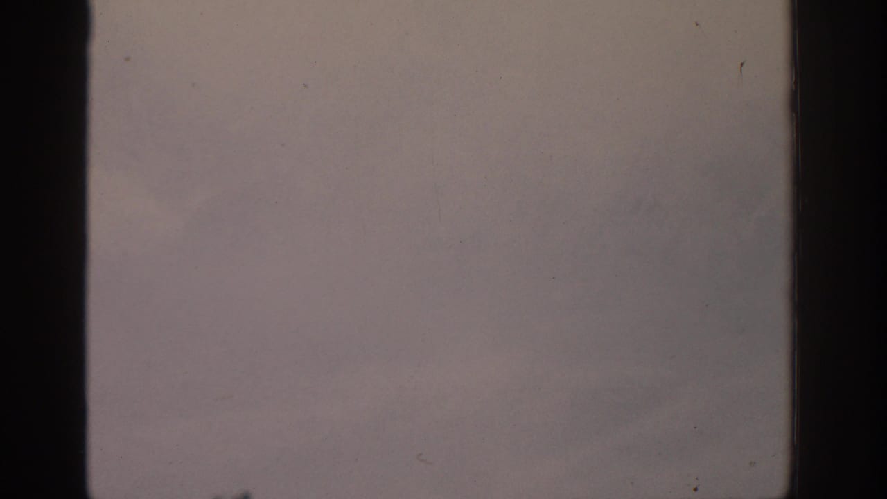1963 8mm frame from the Munich-labeled clip showing a washed, snowy mountain view through dark film borders.