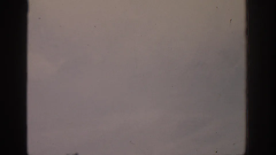 1963 8mm frame from the Munich-labeled clip showing a washed, snowy mountain view through dark film borders.