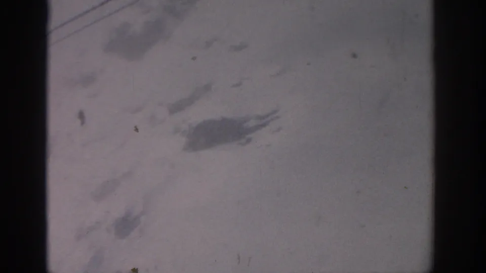 A grainy 1963 8mm view from the Munich-labeled chairlift clip shows snow, faint cables, and dark frame edges.