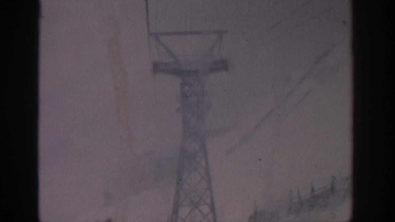 Metal lift tower partly obscured by falling snow and film gate edges.