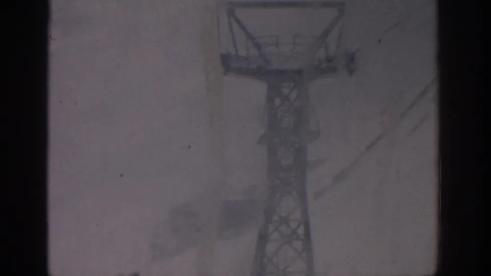 The 8mm frame shows a metal lift tower in Munich, 1963, with snow and film artifacts softening the structure.