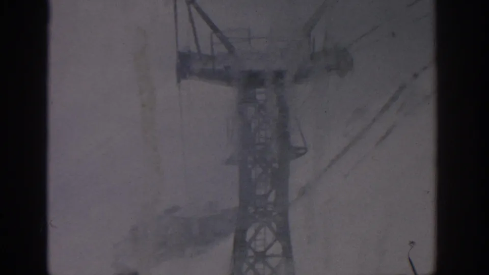 A 1963 Munich home-movie frame captures a metal cable car or ski-lift tower with diagonal lines in heavy snow.