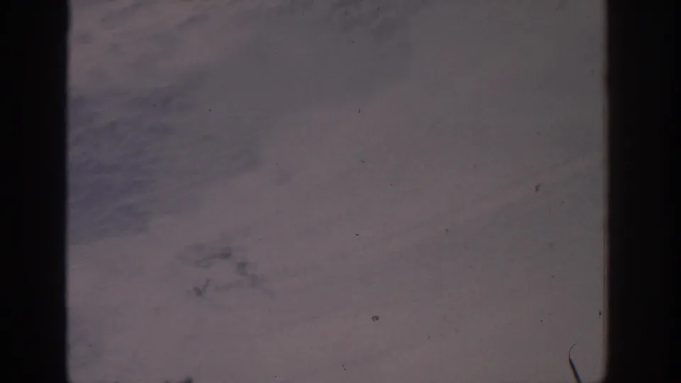 1963 8mm frame of a muted, open landscape with scattered dust marks and dark film-frame borders.