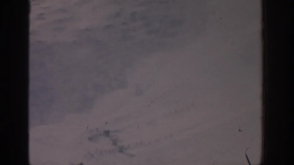 1963 8mm frame showing pale uneven terrain, faint darker areas, and physical-film dust and scratches.