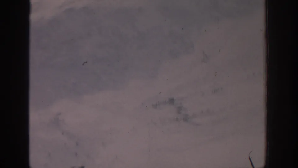 1963 8mm frame of a pale, nearly horizonless landscape with mottled texture and visible film debris.