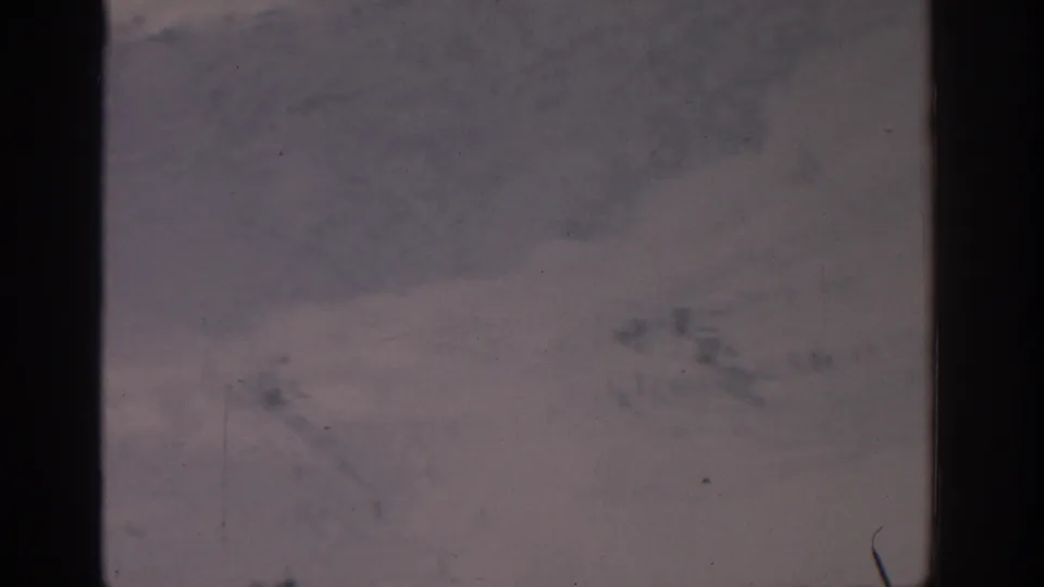 1963 Munich 8mm frame showing an indistinct snow-covered outdoor view with dark gate edges, dust, and soft exposure.