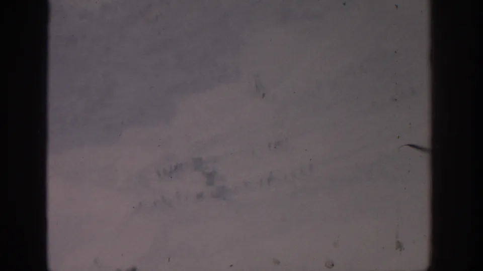 1963 Munich 8mm frame showing a blurred high-angle snow scene with dust, scratches, and dark film-edge intrusion.