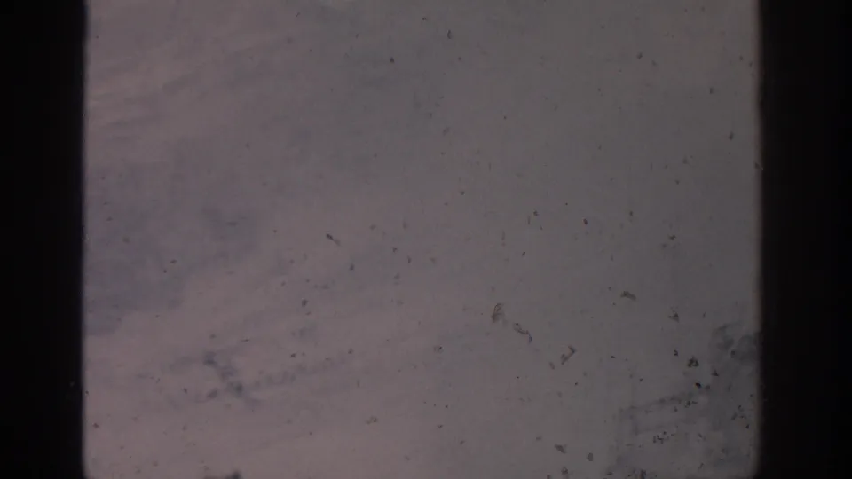 1963 Munich 8mm frame of an indistinct snow-covered area, with visible grain, dust, scratches, and heavy gate-edge shadows.