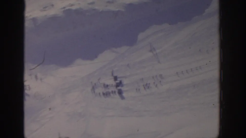 1963 8mm frame from the Munich winter clip with distant figures clustered on a snow-covered hillside.