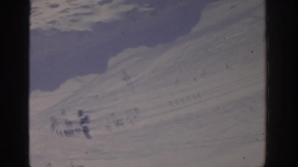 Distant 1963 8mm winter view near Munich with small figures on a snowy slope and soft film blur.