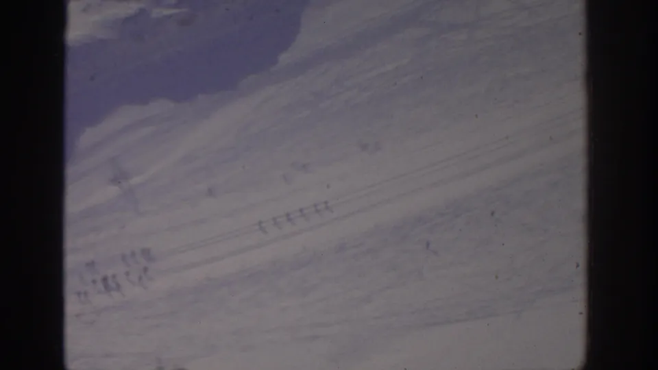 1963 8mm Munich winter snowfield with tiny distant figures and track marks across the slope.
