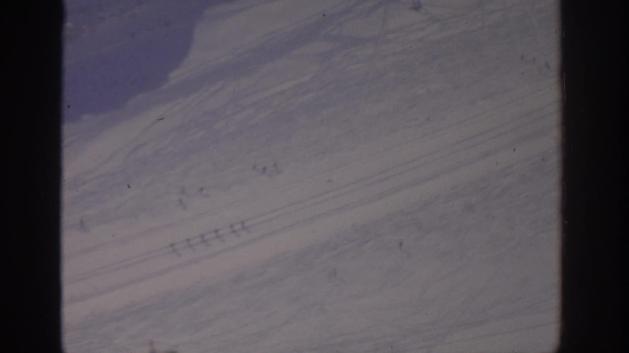Snow-covered slope with many faint parallel tracks and dark film borders.