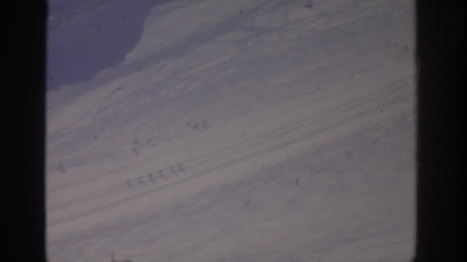 1963 archival 8mm frame, possibly near Munich, showing a broad snowy slope marked by thin trail lines and soft shadowed ridges.