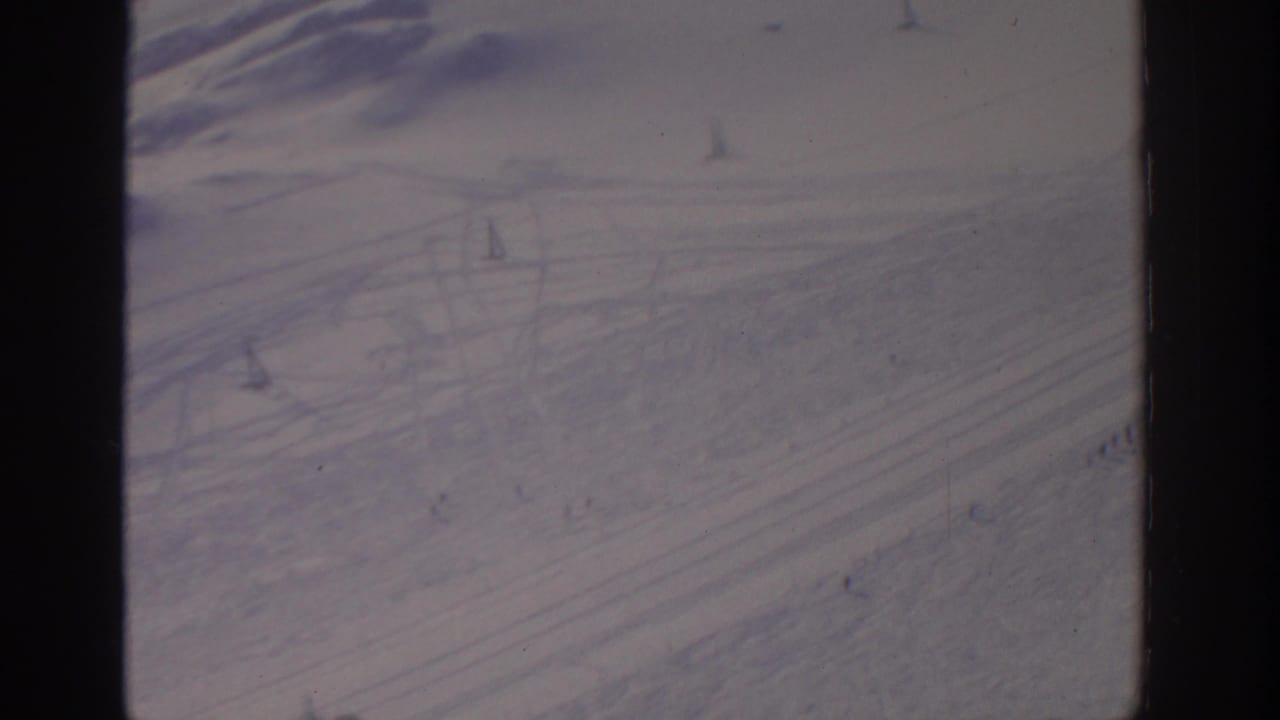 Snowfield with diagonal ski tracks, lift towers, cables, and small figures on the slope.