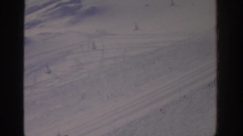 1963 Munich-area winter frame with a pale snowfield, diagonal ski tracks, lift structures, and distant skiers.