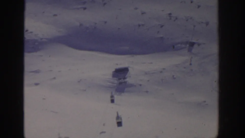 1963 Munich-area ski scene showing a snowy hillside, darker snowbank, scattered tracks, distant skiers, and lift equipment.