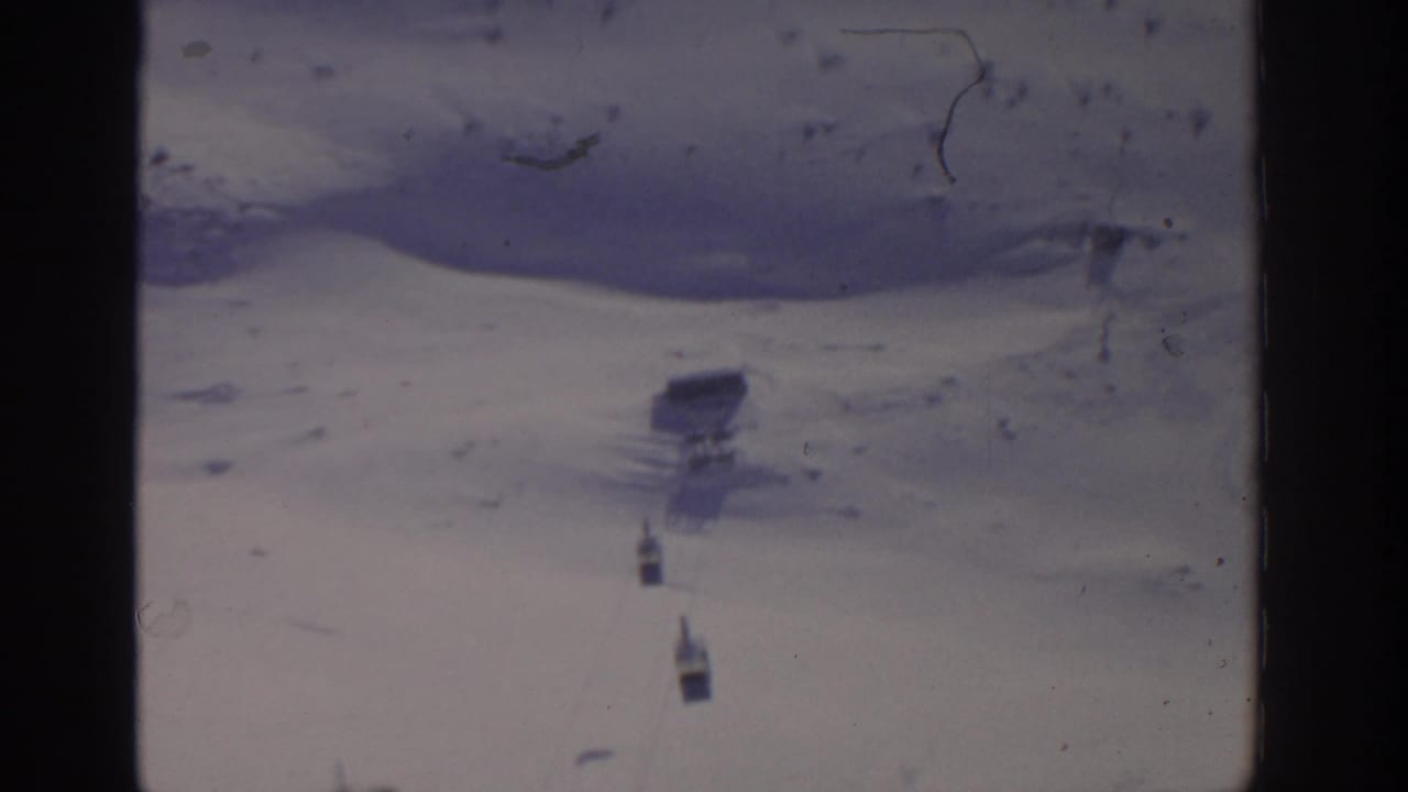 Two small cable car cabins cross a snowy slope beneath faint tram lines.